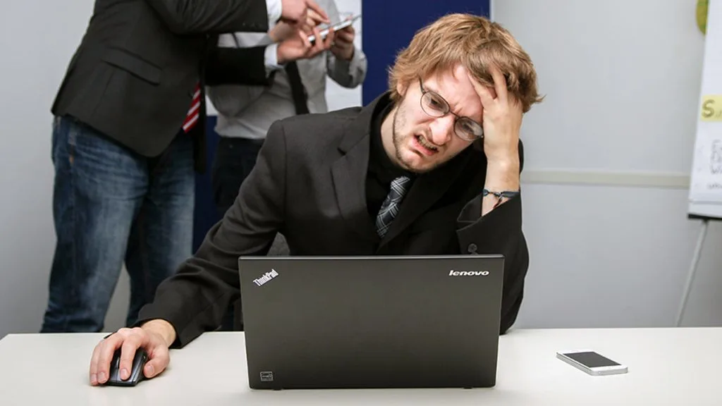 A man on a Lenovo ThinkPad laptop pulling a face because he is frustrated.