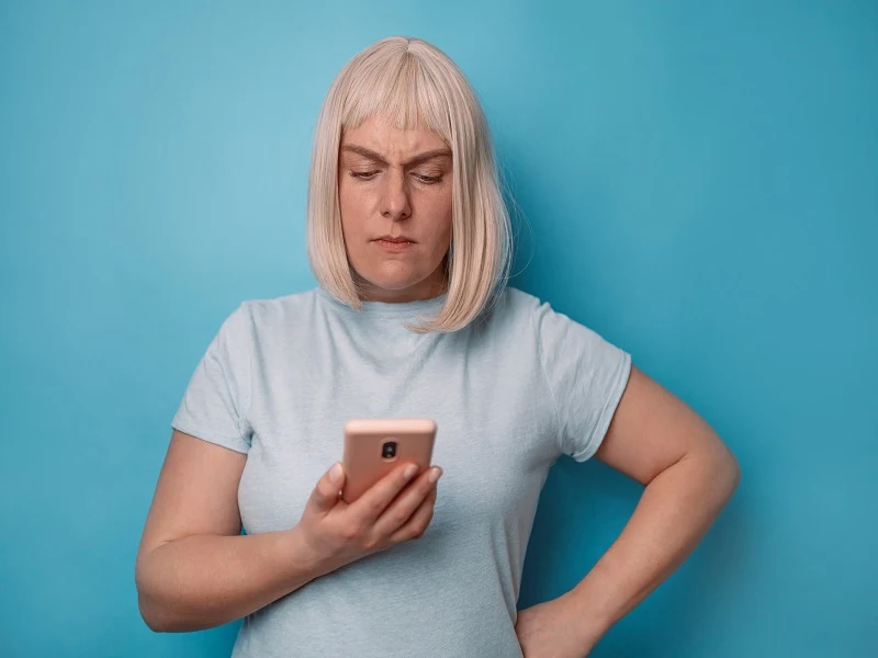 Angry sad european woman holding smartphone having problem with phone on blue background.